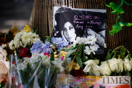 Amy Winehouse Fans Pay Tribute To Late Singer On 10th Anniversary Of Death Amy Winehouse’s family members and fans have gathered at the late singer’s home in North London to pay tribute to her on the 10th anniversary of her death. The musician died on July 23, 2011 at the age of 27 from alcohol poisoning. Pictures have shown a temporary shine situated outside of her house, where supporters have left flowers, balloons and other memorabilia to show their love for Amy. A group of fans also huddled together for a photo, as they posed with two posters which featured images of Amy alongside the words: ‘10 Years Without Amy’. Messages of condolences were also left at the shrine by some, with many expressing their sadness at how long it has been since the singer has gone. Other photos show fans standing alongside Amy’s statue, which is situated in Camden Town.